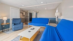 A modern room with a sofa, a small table, and a kitchen area in the background. - Ocean Air Suites 300 Feet from Beach, Strip (Hampton)