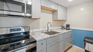 A modern kitchen with stainless steel appliances, a granite countertop, and light grey cabinetry. - Ocean Air Suites 300 Feet from Beach, Strip (Hampton)