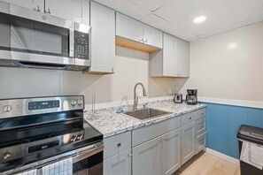 A modern kitchen with stainless steel appliances, a granite countertop, and light grey cabinetry. - Ocean Air Suites 300 Feet from Beach, Strip (Hampton)