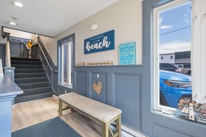 A staircase leading to a landing with a bench, a wall with decorative signs, and a view of a blue car outside. - Ocean Air Suites 300 Feet from Beach, Strip (Hampton)