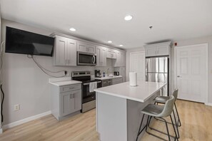 A modern kitchen with white cabinets, stainless steel appliances, a flat-screen TV, and a bar area with stools. - Ocean Air Suites 300 Feet from Beach, Strip (Hampton)