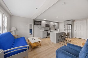 A compact living space with a kitchenette, a sofa, a small table, and a TV mounted on the wall. - Ocean Air Suites 300 Feet from Beach, Strip (Hampton)