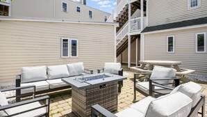 Eine Terrasse mit Gartenmöbeln, einem Feuerkorb und einer Treppe zu einer oberen Ebene.