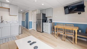 A modern kitchen with white cabinets, a stainless steel refrigerator, a coffee maker, and a dining area with a wooden table and chairs. - Ocean Air Suites 300 Feet from Beach, Strip (Hampton)