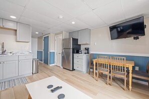 A modern kitchen with white cabinets, a stainless steel refrigerator, a coffee maker, and a dining area with a wooden table and chairs. - Ocean Air Suites 300 Feet from Beach, Strip (Hampton)