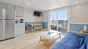 A compact kitchen with a refrigerator, a dining table with chairs, a coffee maker, and a television mounted on the wall. - Ocean Air Suites 300 Feet from Beach, Strip (Hampton)