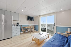 A compact kitchen with a refrigerator, a dining table with chairs, a coffee maker, and a television mounted on the wall. - Ocean Air Suites 300 Feet from Beach, Strip (Hampton)