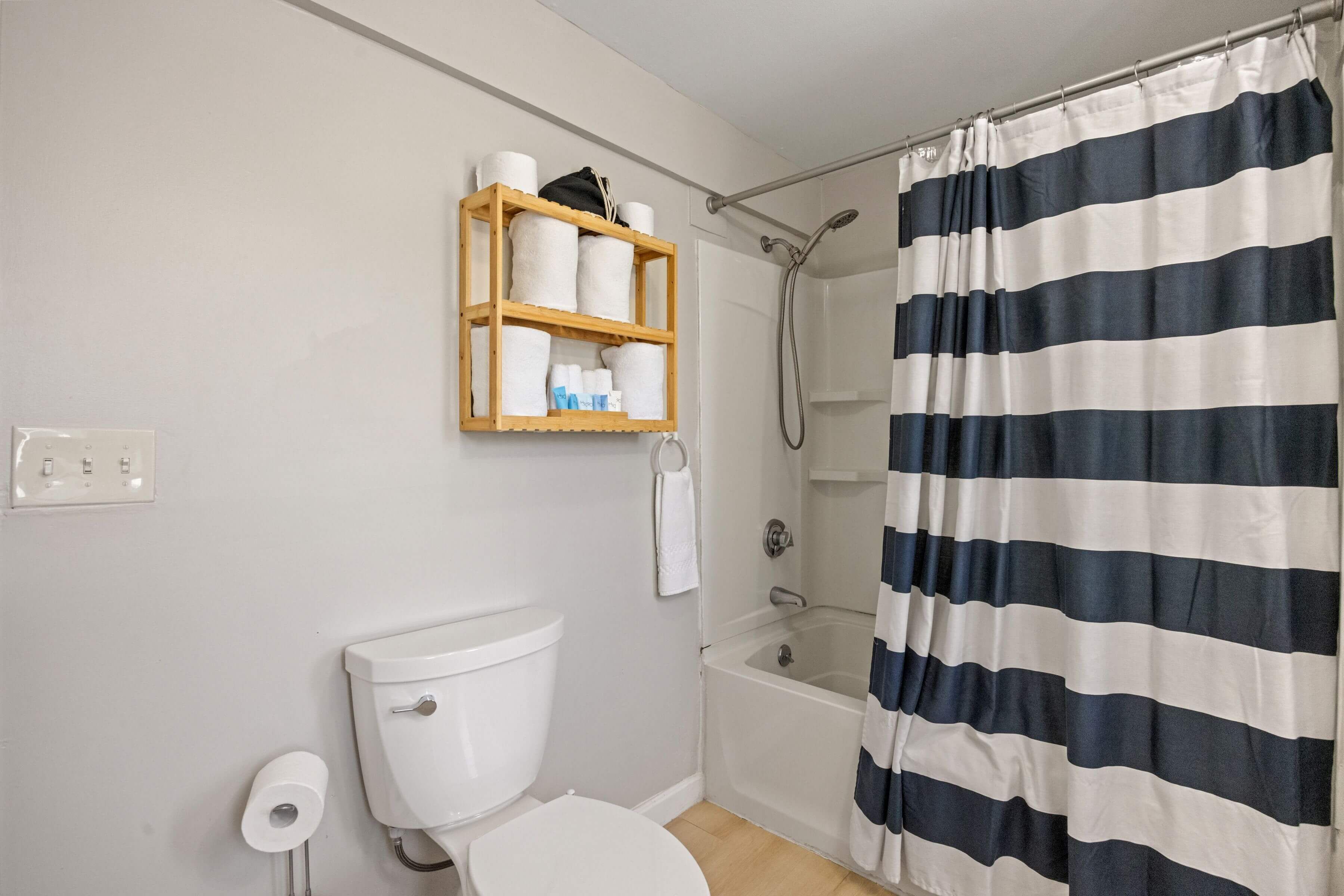A bathroom with a toilet, a shower, a bathtub, a wooden shelf with toiletries, and a striped shower curtain.