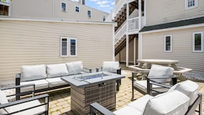 Eine Terrasse mit Gartenmöbeln, einem Feuerkorb und einer Treppe zu einer oberen Ebene.