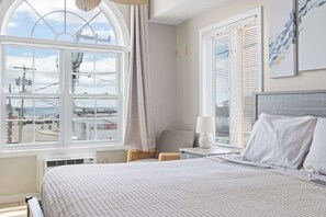 A hotel room with a large window, a bed, a chair, a nightstand, and a lamp. - Ocean Air Suites 300 Feet from Beach, Strip (Hampton)