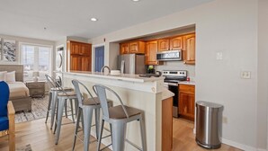 A modern kitchen with wooden cabinets, stainless steel appliances, and a bar area with stools. - Ocean Air Suites 300 Feet from Beach, Strip (Hampton)