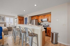 A modern kitchen with wooden cabinets, stainless steel appliances, and a bar area with stools. - Ocean Air Suites 300 Feet from Beach, Strip (Hampton)