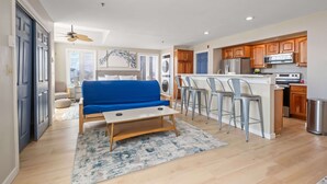 A compact living space with a kitchenette, a blue sofa, a small table, and a ceiling fan. - Ocean Air Suites 300 Feet from Beach, Strip (Hampton)