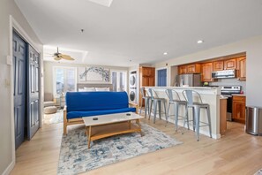 A compact living space with a kitchenette, a blue sofa, a small table, and a ceiling fan. - Ocean Air Suites 300 Feet from Beach, Strip (Hampton)