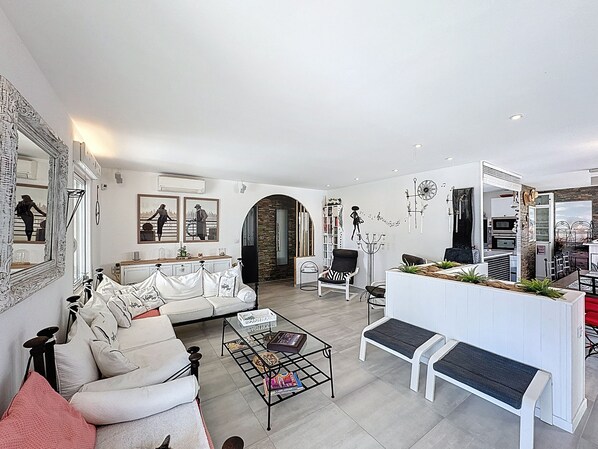 A modern living room with a white sofa, a coffee table, and a dining area with a white bench.