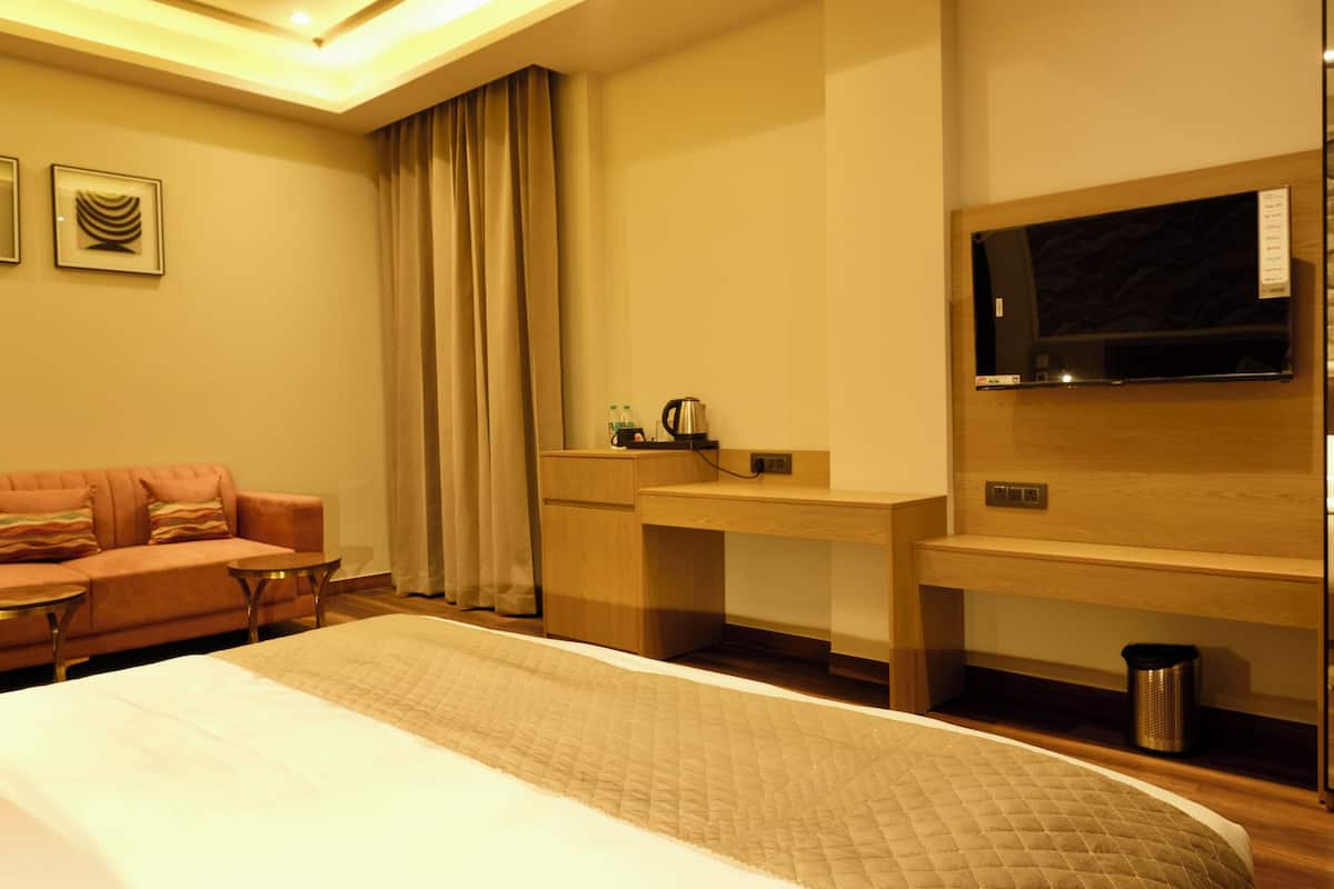 Una habitación de hotel con cama, escritorio, televisión, sofá y cafetera.