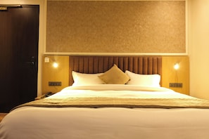 A hotel room with a bed, a wooden headboard, bedside lamps, and a door. - Red Sapphire Royal (Moradabad)