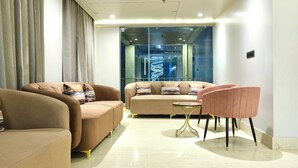 A modern living room with two sofas, a pink chair, and a small round table. - Red Sapphire Royal (Moradabad)