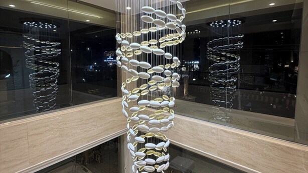 A modern interior with a spiral light fixture, glass railings, and a view of the cityscape. - Red Sapphire Royal (Moradabad)