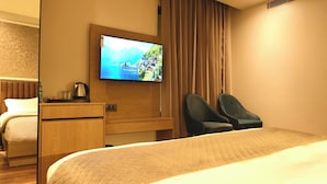 A hotel room with a bed, a TV mounted on the wall, a desk with a kettle, and two chairs. - Red Sapphire Royal (Moradabad)