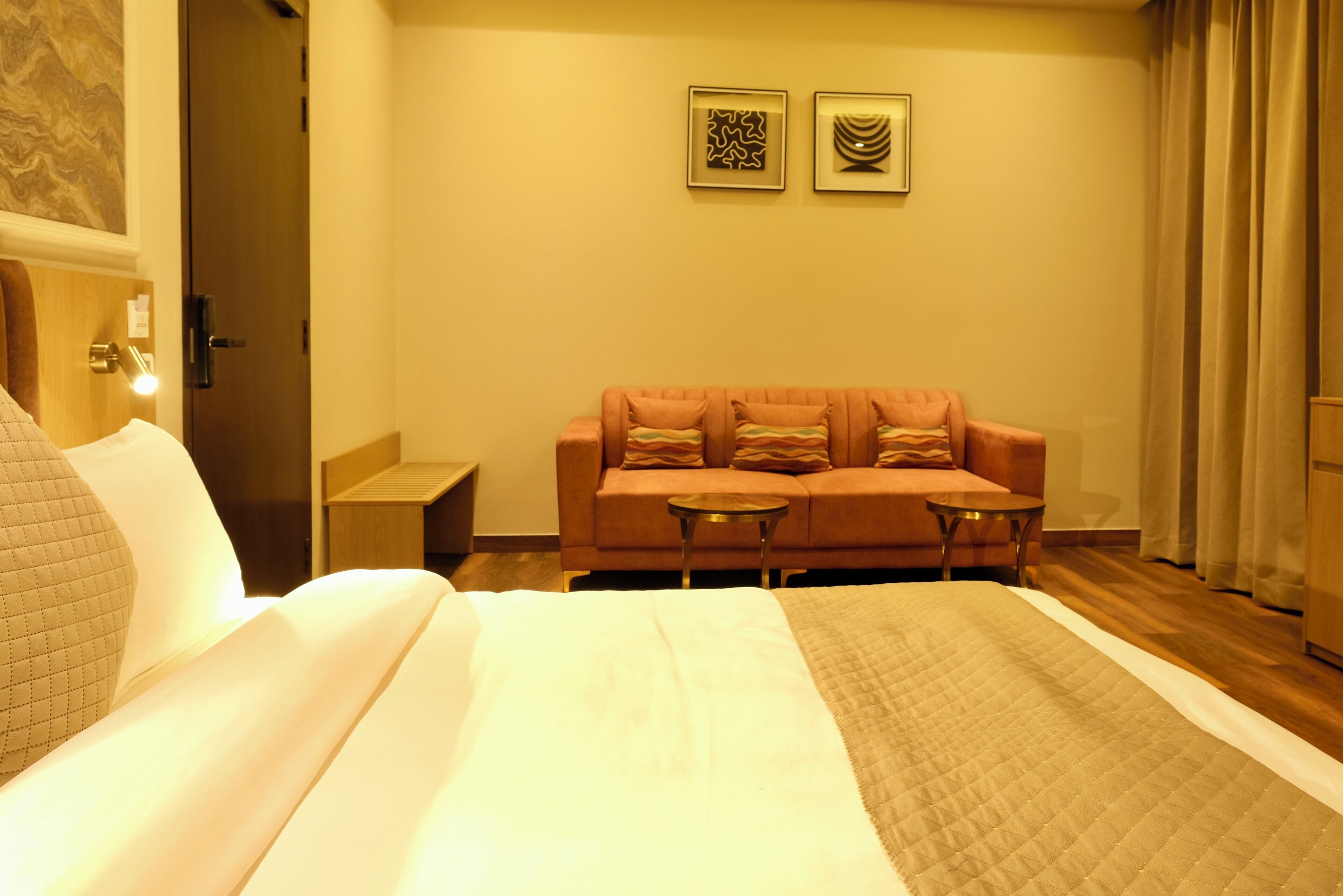 A hotel room with a bed, a sofa, a small table, and two framed pictures on the wall.