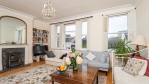 A living room with a fireplace, sofa, coffee table, and a bookshelf. - The Warwick Avenue Retreat, by Veeve (London)