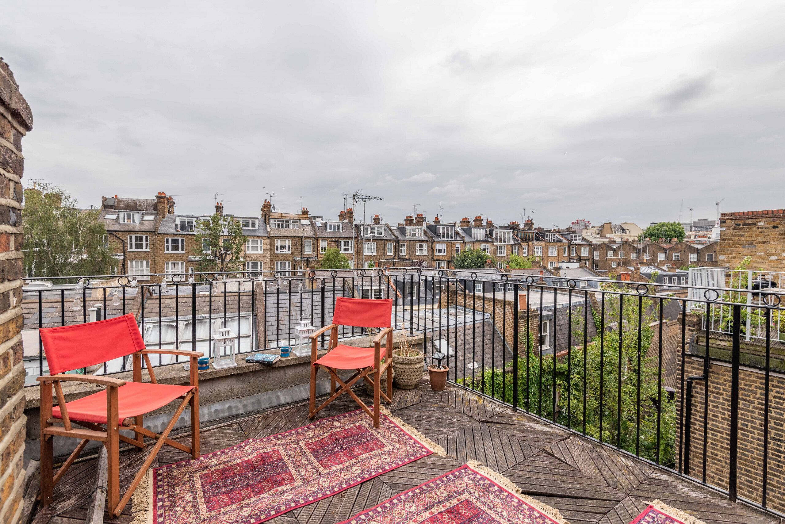 Une terrasse sur le toit avec deux chaises en bois, un coussin rouge et un tapis à motifs.