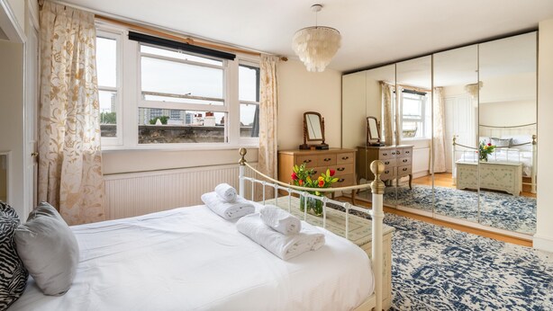 A bedroom with a bed, a dresser, a mirror, and a window with curtains. - The Warwick Avenue Retreat, by Veeve (London)