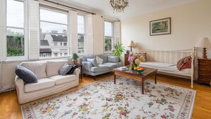 A living room with a sofa, a coffee table, a lamp, and a painting on the wall. - The Warwick Avenue Retreat, by Veeve (London)