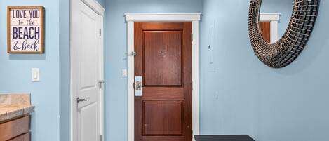 A hallway with a wooden door, a mirror, and a sign on the wall.