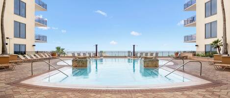 Un área de piscina con vista al océano, rodeada de sillas de descanso y un suelo de baldosas.