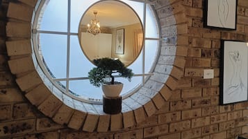 A round mirror with a potted plant, a chandelier, and framed artwork on a brick wall.