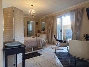 Un dormitorio con cama, mesita de noche, silla y vista al exterior.