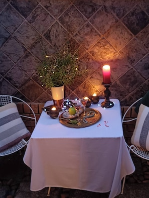Menja a l'aire lliure amb una taula, espelmes, una planta en test i un plat amb aliments.