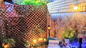 Un espace de restauration en plein air avec une table dressée pour deux personnes, entouré d’une clôture rustique et de plantes en pot.