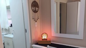 Une pièce avec un bureau blanc, un miroir, un attrape-rêves accroché au mur et un panier en osier.