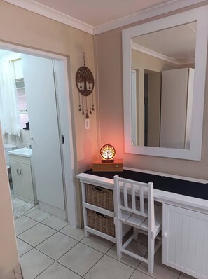 Una habitació amb escriptori blanc, mirall, penjador somni i cistella de vímet.