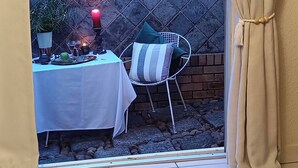 Un espace patio aménagé avec une table dressée pour les repas, une chaise et un petit jardin.