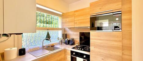A modern kitchen with wooden cabinets, a Bosch oven, a sink, and a window with a view of greenery.