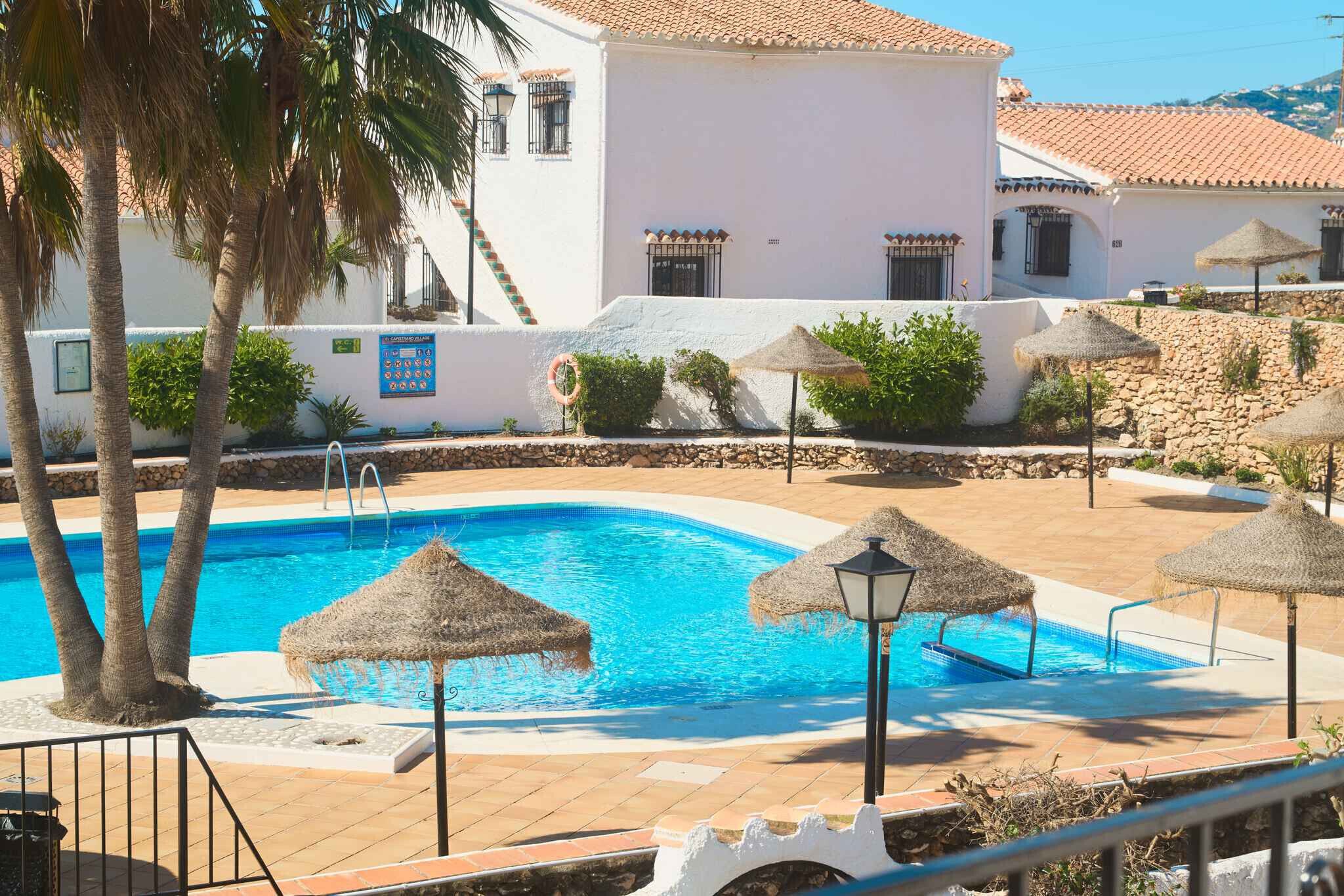 A swimming pool with thatched umbrellas, palm trees, and a white building with a tiled roof.