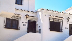 Un bâtiment blanc avec des barreaux noirs aux fenêtres, portant les numéros 110B et 111B, et un petit balcon doté d’une rambarde en métal.