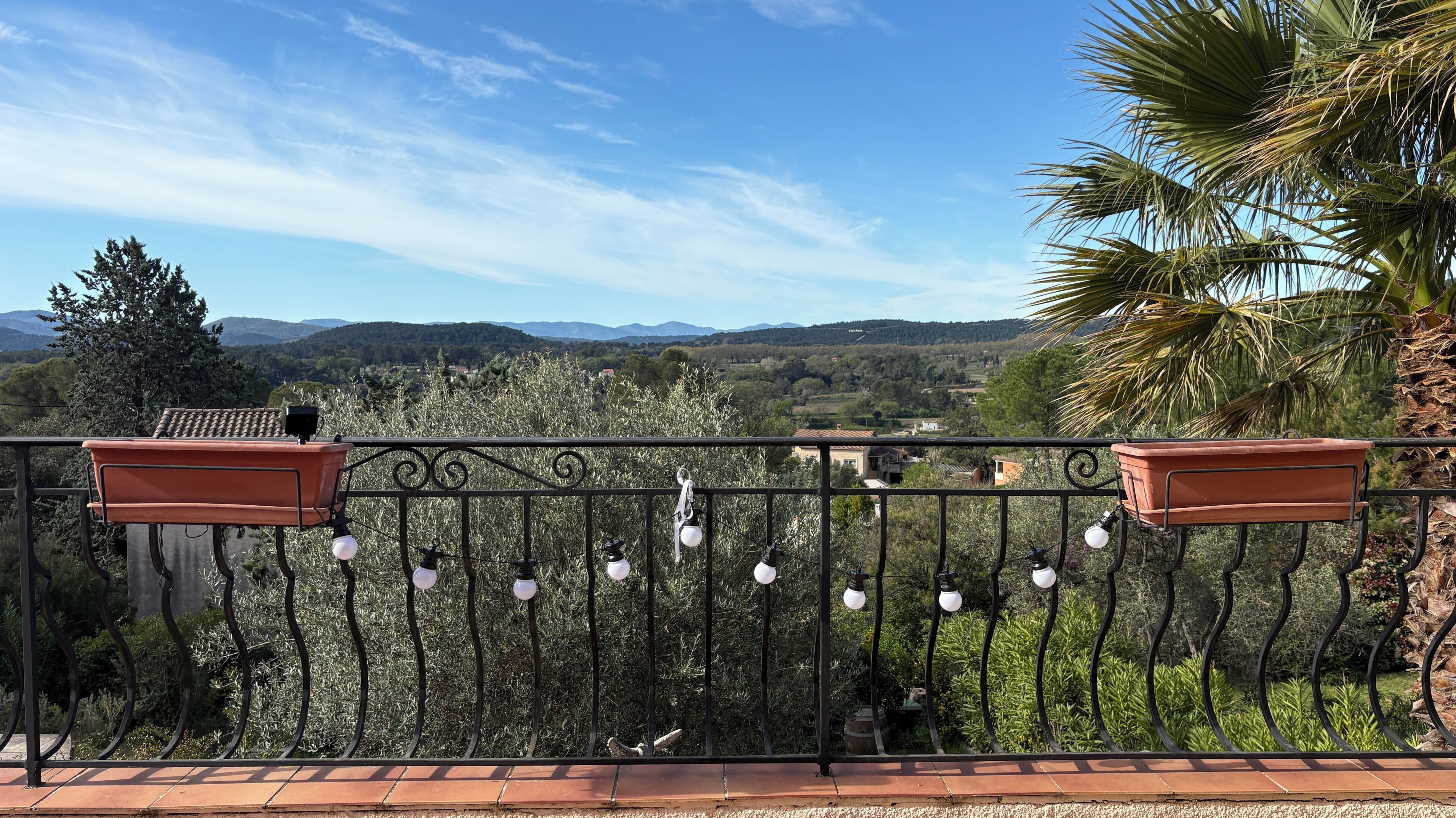 A balcony with a view of a rural landscape, including trees and distant hills.