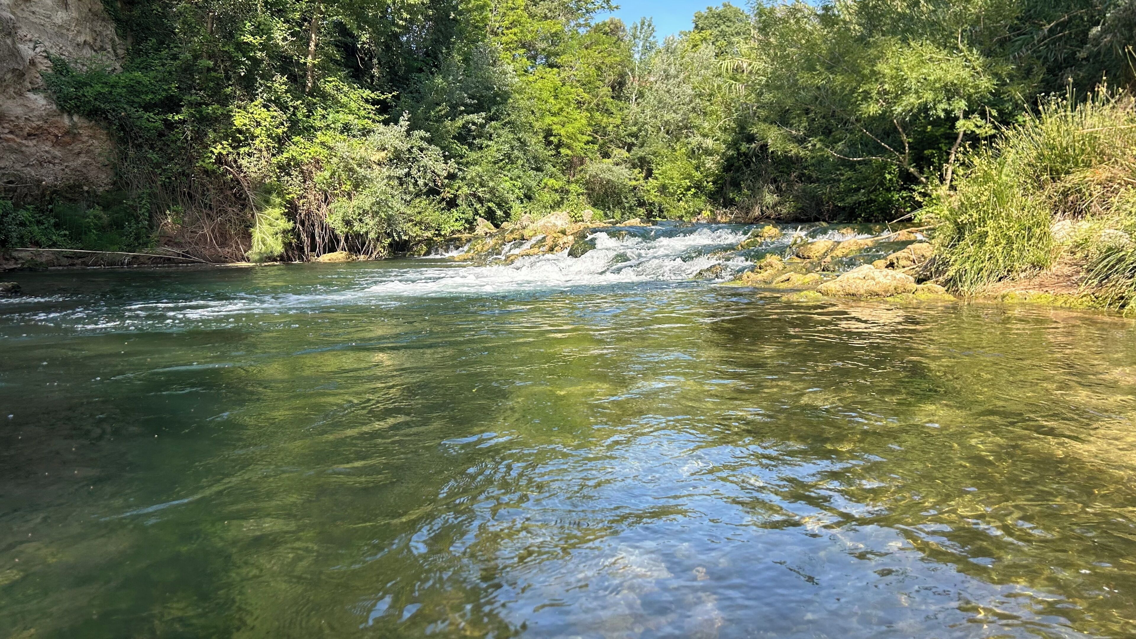 Un río de aguas cristalinas, rodeado de abundante vegetación y terreno rocoso.