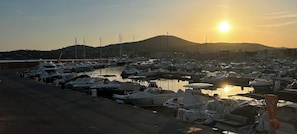 Uma marina com barcos atracados, céu claro e montanha ao fundo.
