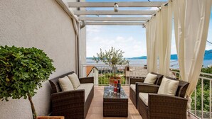 Ein Balkon mit Korbmöbeln, einer Topfpflanze und Blick aufs Meer.