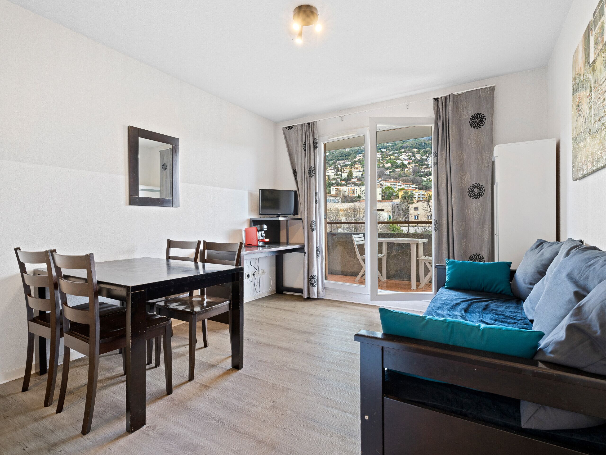 Et værelse med et spisebord, stole, et fjernsyn, en sofa og en balkon med udsigt.