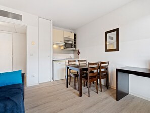 Ein kompakter Wohnraum mit Küchenzeile, Essbereich und kleinem Schreibtisch.