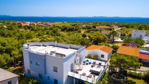 Um edifício moderno com terraço no telhado, rodeado por vegetação exuberante e vista para o mar.