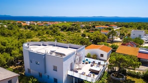A modern building with a rooftop terrace, surrounded by lush greenery and a view of the sea. - Apartman Elemar by Villas Guide (Vir)