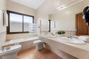A modern bathroom with a toilet, bidet, two sinks, a large mirror, and a window. - Villa Dafne by Escape Home (Playa Blanca)